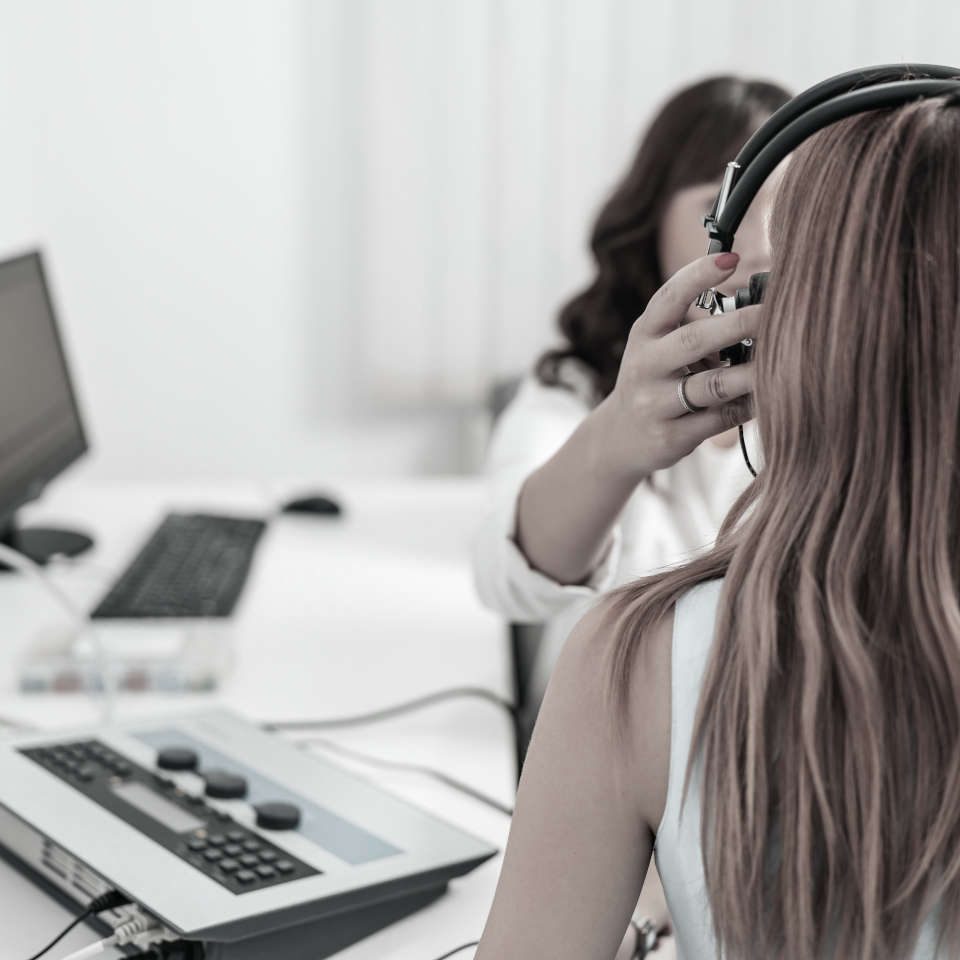 A person wearing headphones during a hearing test, with the audiometer in the foreground